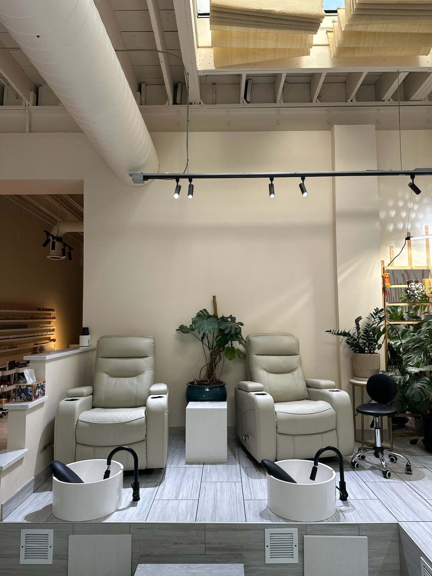 Two pedicure chairs with a monstera plant beneath the high salon ceiling